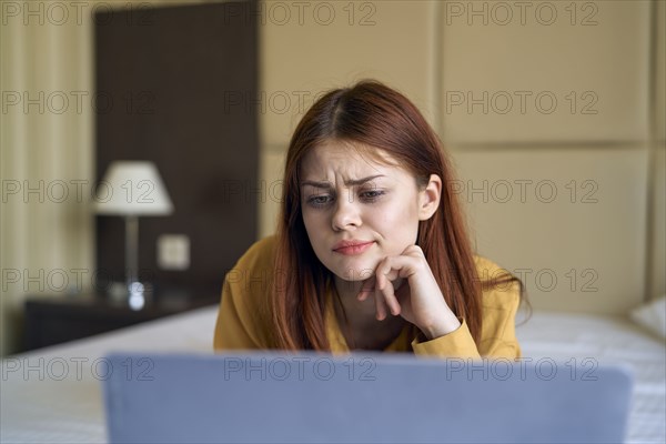 Confused Caucasian woman laying on bed using laptop