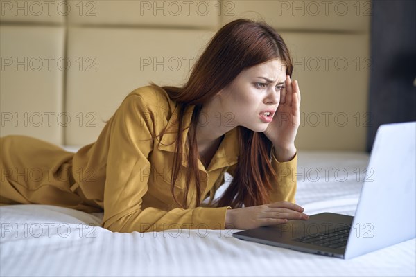 Frustrated Caucasian woman laying on bed using laptop