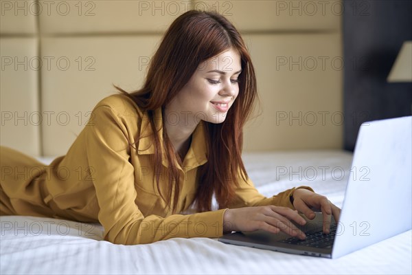 Smiling Caucasian woman laying on bed using laptop