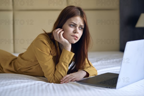 Confused Caucasian woman laying on bed using laptop