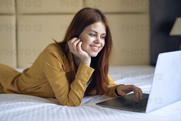 Smiling Caucasian woman laying on bed using laptop