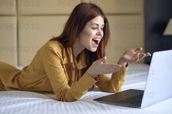 Excited Caucasian woman laying on bed using laptop