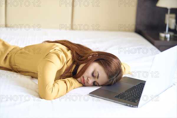 Fatigued Caucasian woman sleeping on bed near laptop