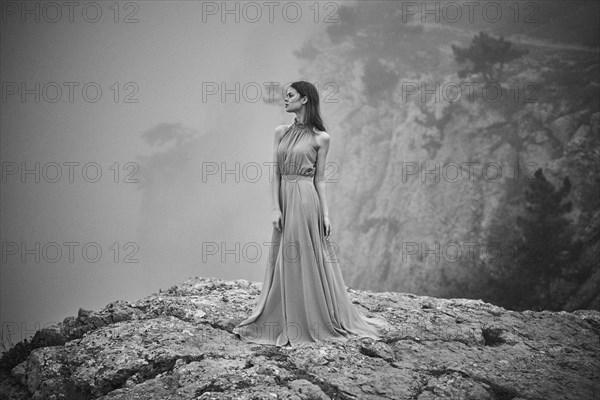 Woman wearing dress standing on rock in fog