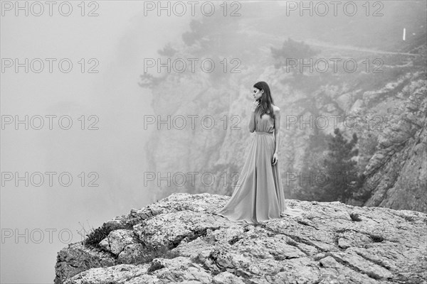 Woman wearing dress standing on rock in fog