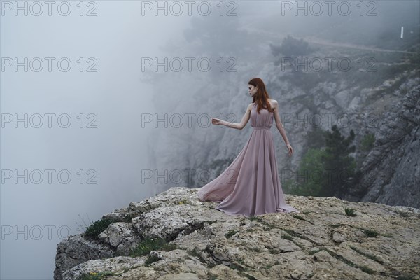 Woman wearing dress standing on rock in fog