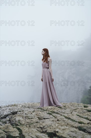 Caucasian woman wearing dress on rock in fog