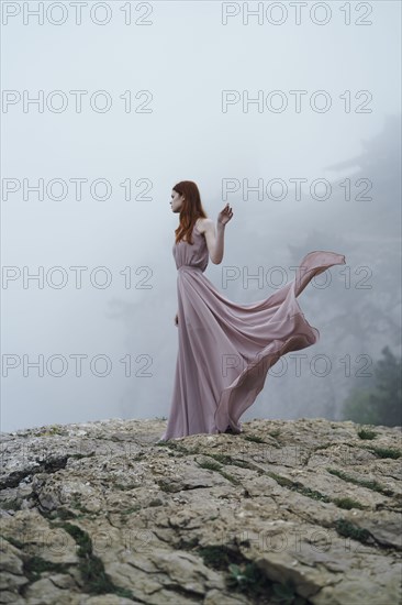 Caucasian woman wearing dress on rock in fog
