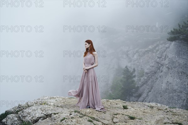 Caucasian woman wearing dress on rock in fog