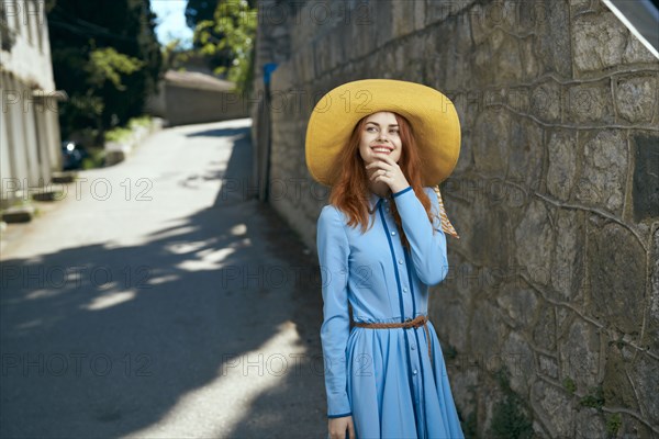 Smiling Caucasian woman wearing hat near stone wall