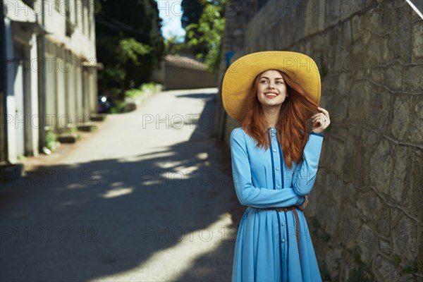 Smiling Caucasian woman wearing hat near stone wall