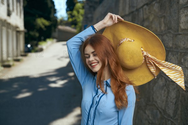 Smiling Caucasian woman holding hat near stone wall