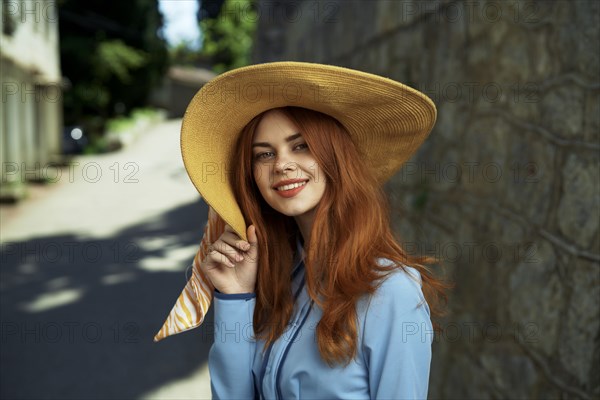 Smiling Caucasian woman wearing hat near stone wall