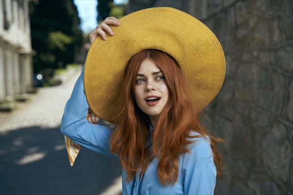 Surprised Caucasian woman holding hat near stone wall