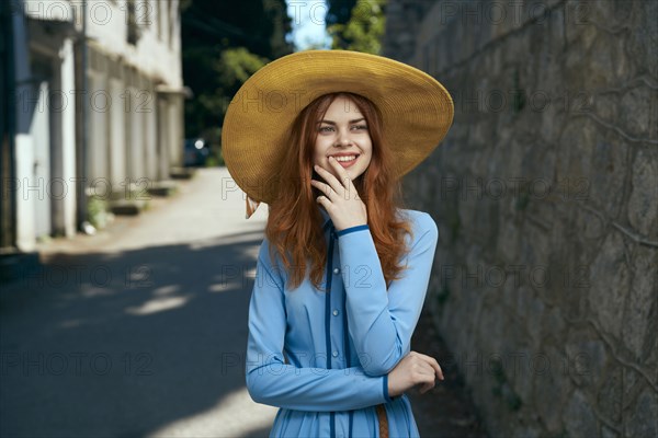 Smiling Caucasian woman wearing hat near stone wall