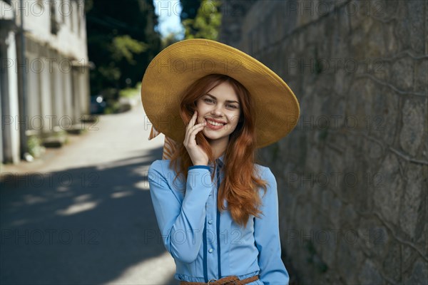 Smiling Caucasian woman wearing hat near stone wall