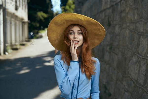 Surprised Caucasian woman wearing hat near stone wall