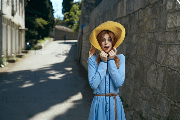 Surprised Caucasian woman wearing hat near stone wall