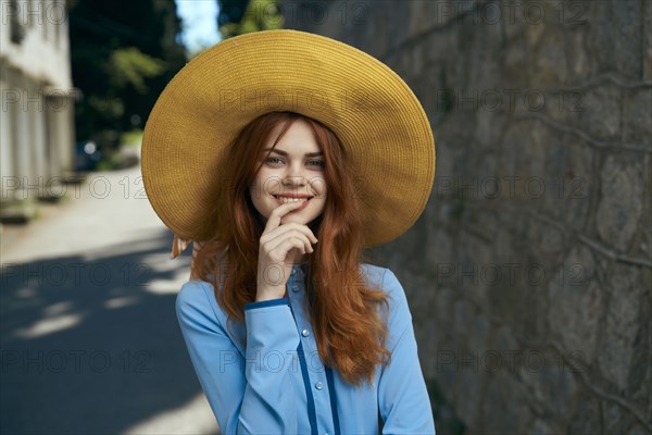 Smiling Caucasian woman wearing hat near stone wall