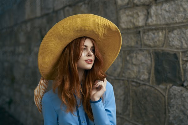 Smiling Caucasian woman wearing hat near stone wall