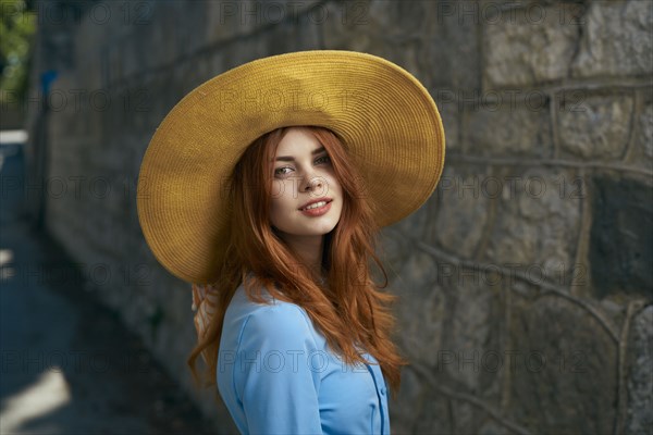 Smiling Caucasian woman wearing hat near stone wall