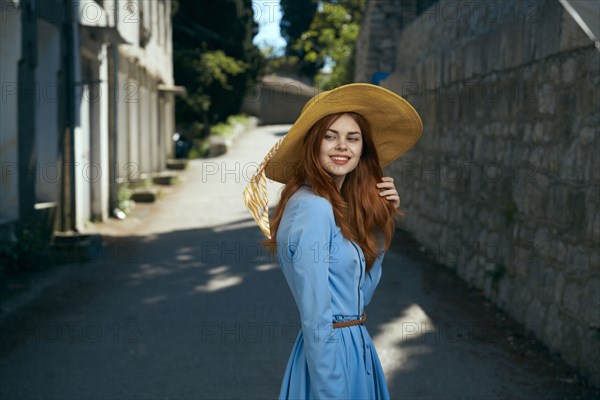 Smiling Caucasian woman wearing hat near stone wall