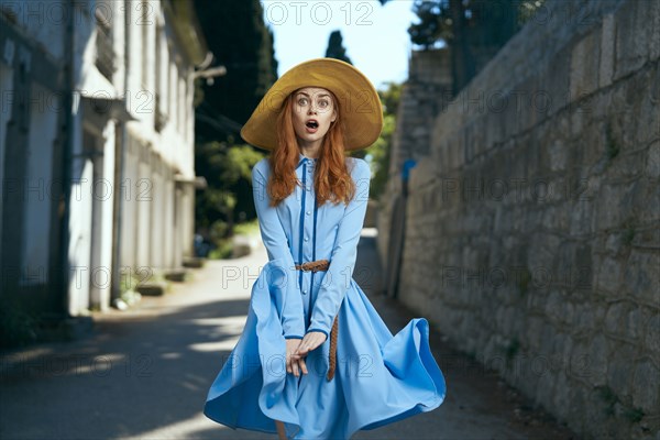 Surprised Caucasian woman wearing hat near stone wall