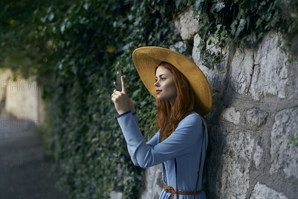 Caucasian woman photographing with cell phone near stone wall