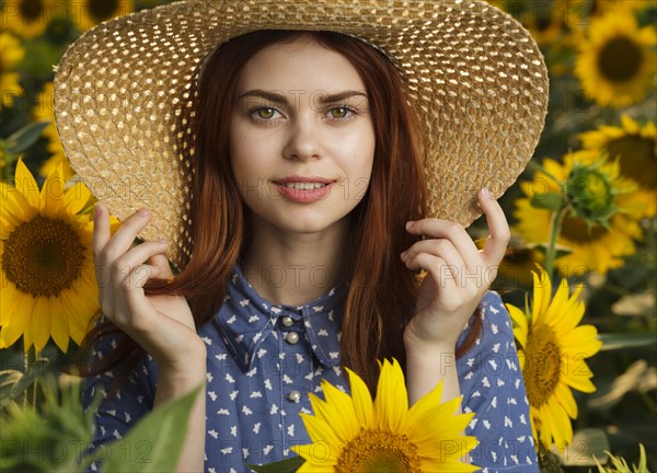 Smiling Caucasian woman wearing hat in field of sunflowers