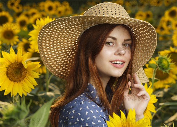 Smiling Caucasian woman wearing hat in field of sunflowers