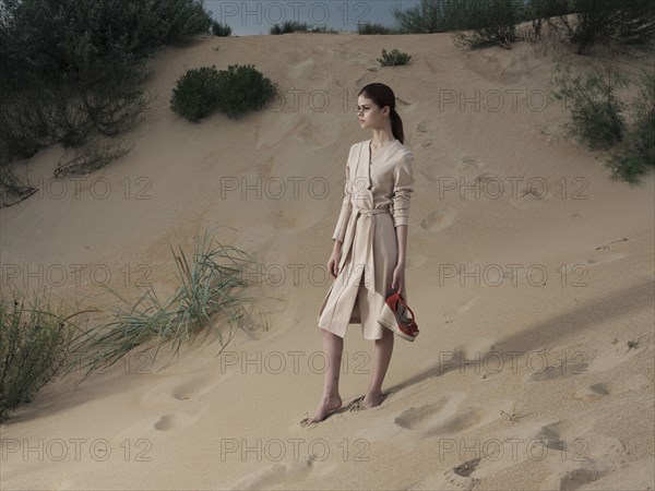 Caucasian woman wearing dress on beach carrying shoes