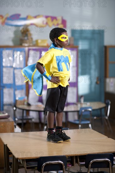 African American boy in superhero costume standing on desk