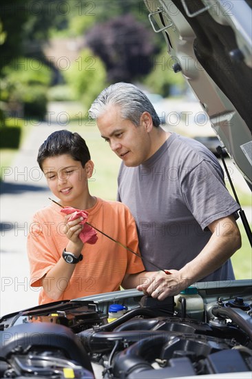 Hispanic father and son checking oil in car