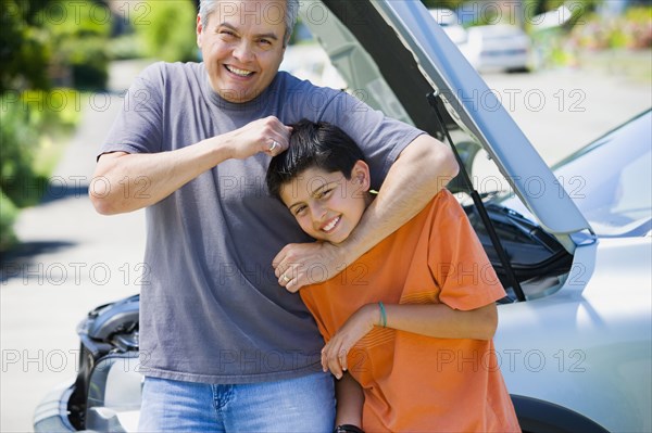 Hispanic father and son playing in front of car with hood up