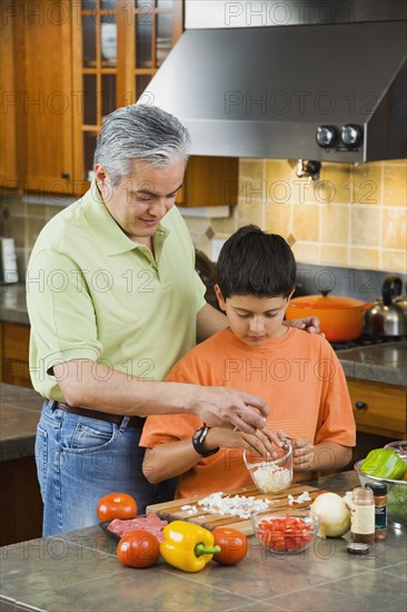 Hispanic father and son chopping vegetables in kitchen