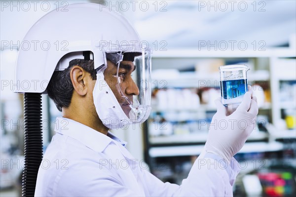 Indian male scientist wearing respirator and looking at beaker