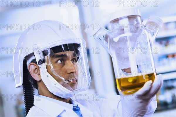 Indian male scientist wearing respirator and looking at beaker