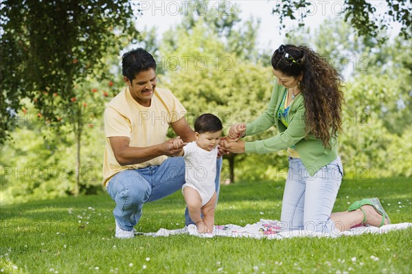 Hispanic parents helping baby walk in park