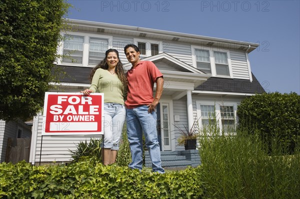 Hispanic couple with For Sale sign in front of house