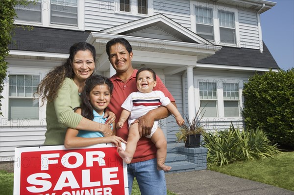 Hispanic family with For Sale sign in front of house
