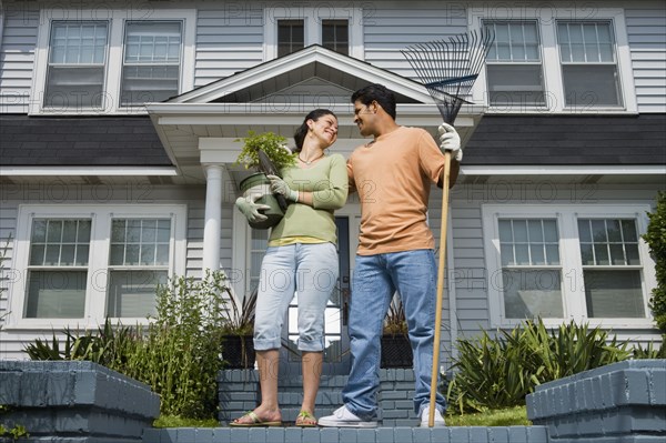 Hispanic couple with gardening tools in front of house