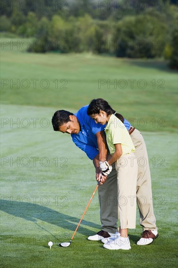 Hispanic father helping daughter play golf