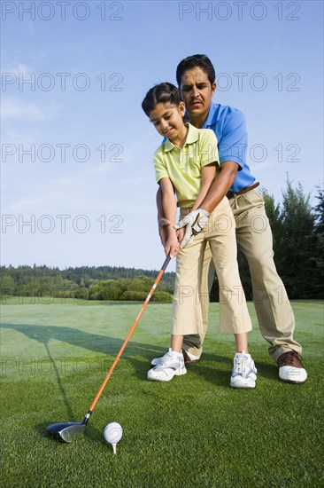 Hispanic father helping daughter play golf