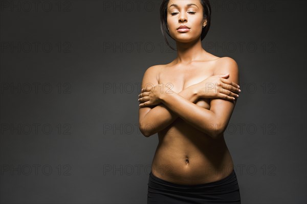 Semi-nude Hispanic woman with eyes closed and arms covering breasts