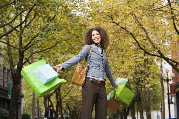 Hispanic woman swinging shopping bags in urban park