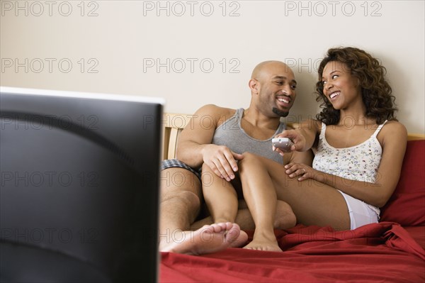 African couple watching television in bed