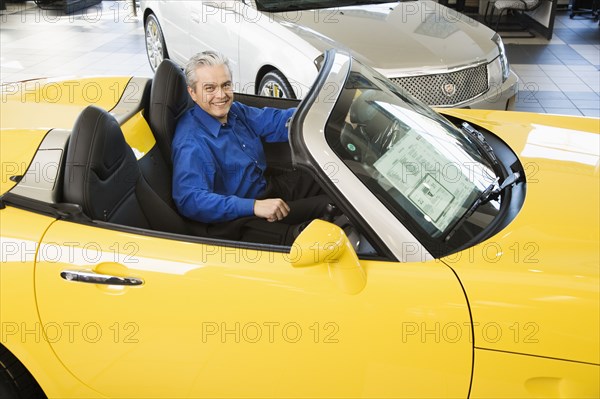 Hispanic car salesman sitting in new car