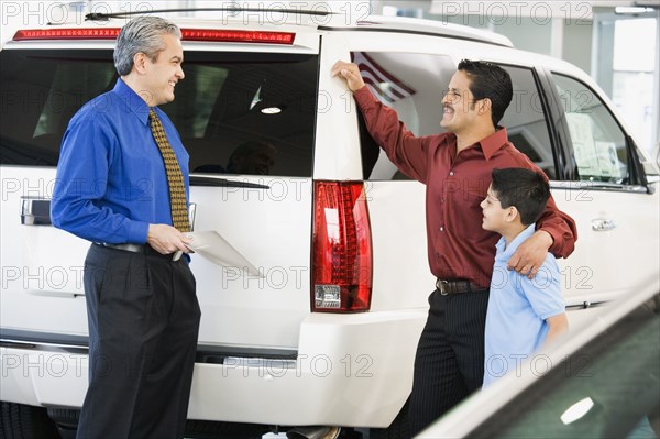 Hispanic car salesman talking to father and son