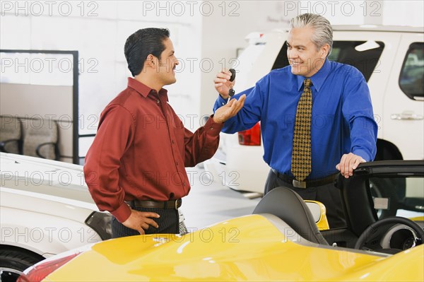 Hispanic car salesman handing car keys to buyer