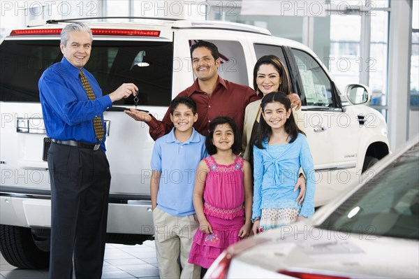 Hispanic car salesman handing car keys to family